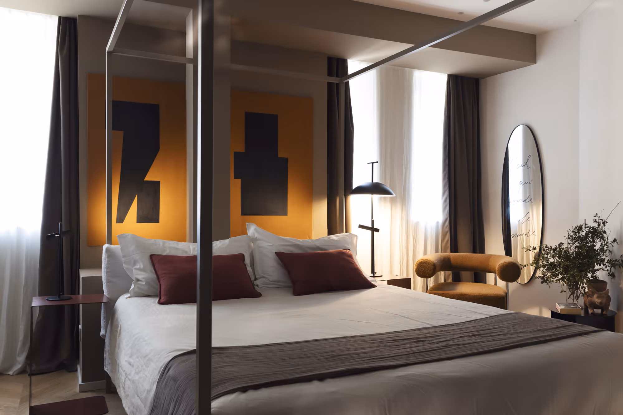 Camera con letto a baldacchino in ferro, cuscini bordeaux e un grande quadro astratto