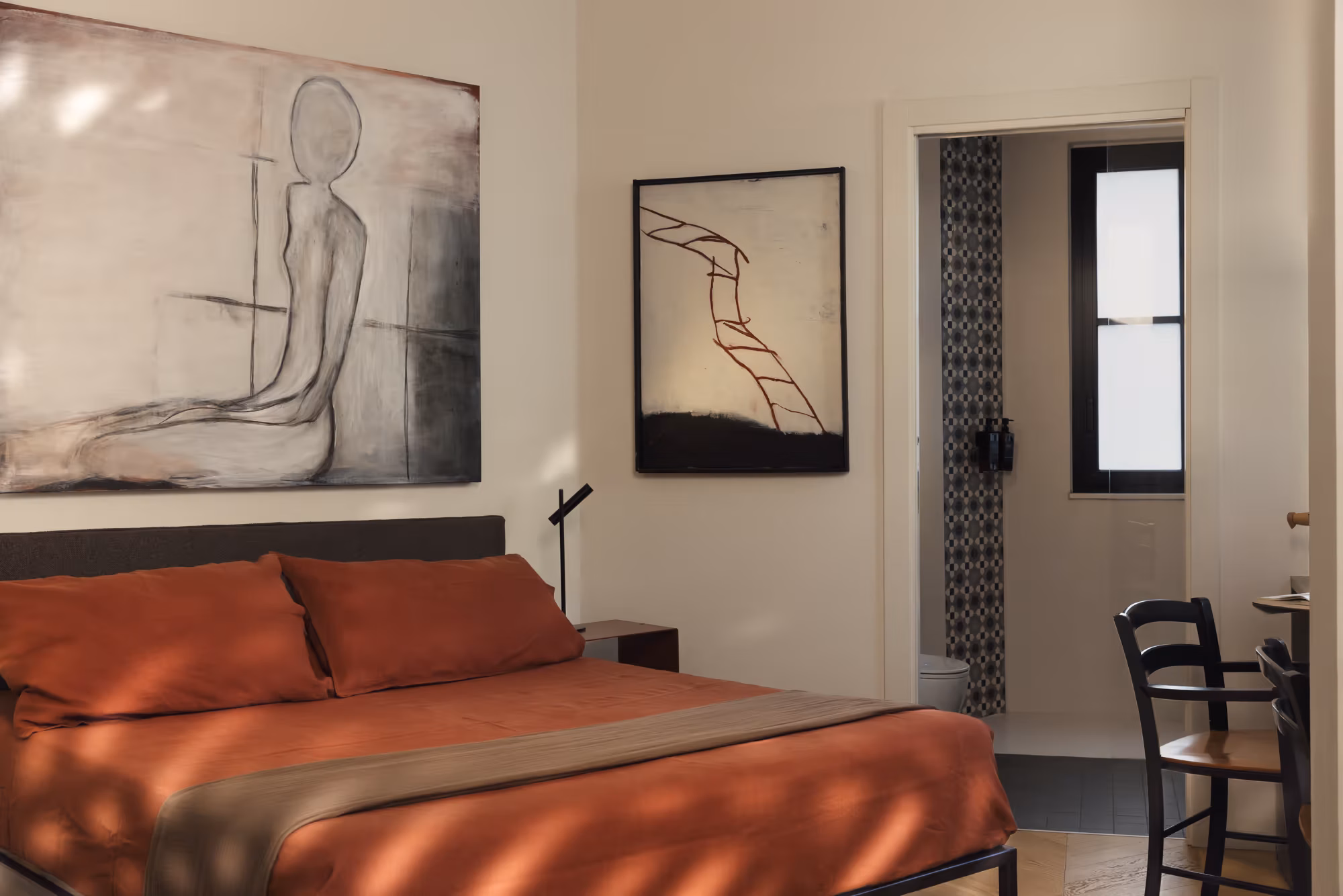 Camera con copriletto rosso mattone e due disegni incorniciati sopra il letto