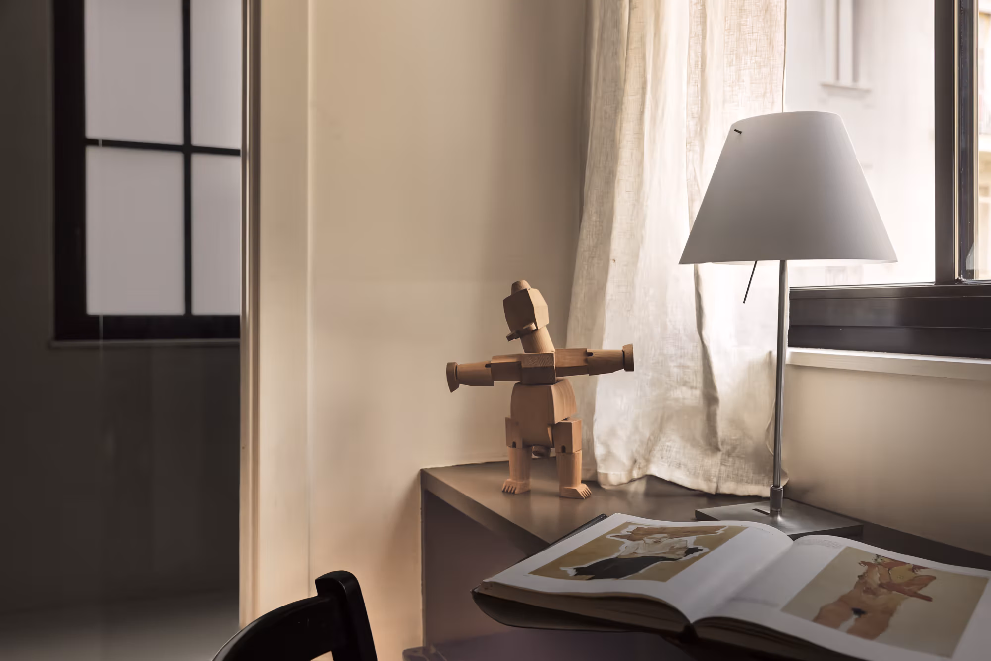 Lampada accesa su una mensola, un libro d'arte aperto e una scultura in legno