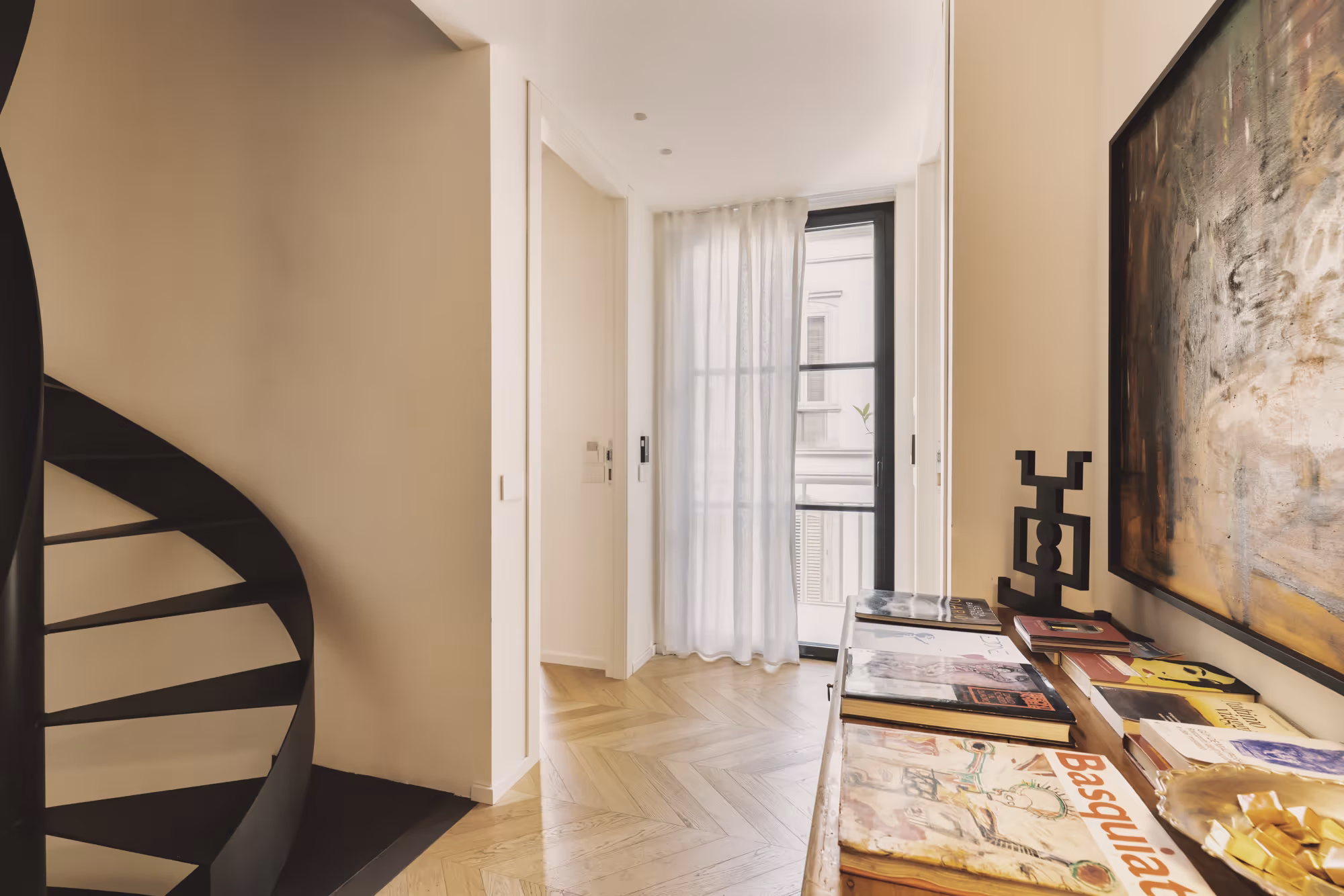 Corridoio con parquet a spina di pesce, scala a chiocciola nera e libri d'arte su una consolle